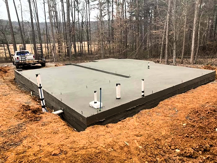 New construction concrete slab with plumbing stub-outs at a wooded building site
