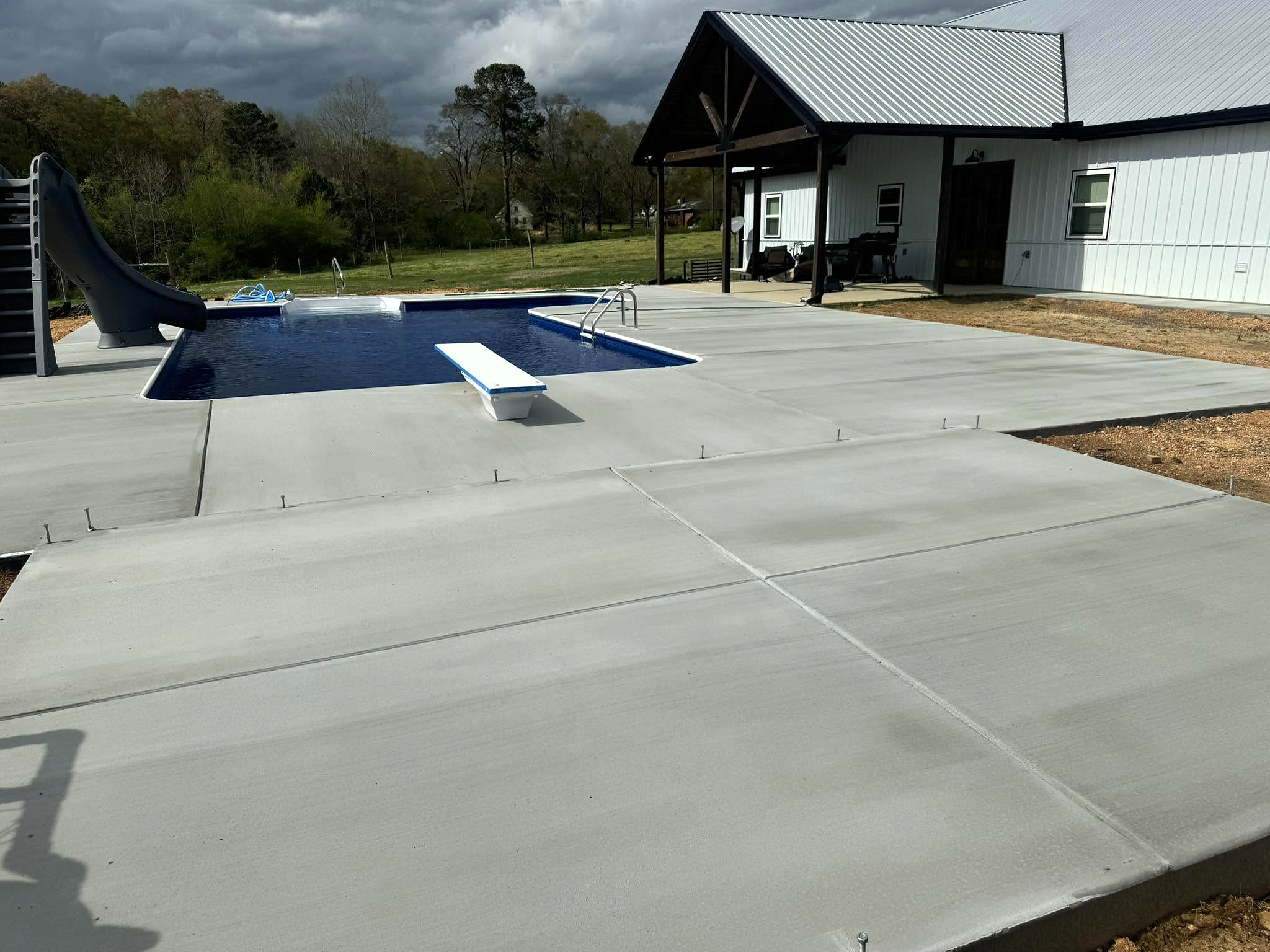 Wide concrete pool deck surrounding a residential swimming pool beside a covered porch