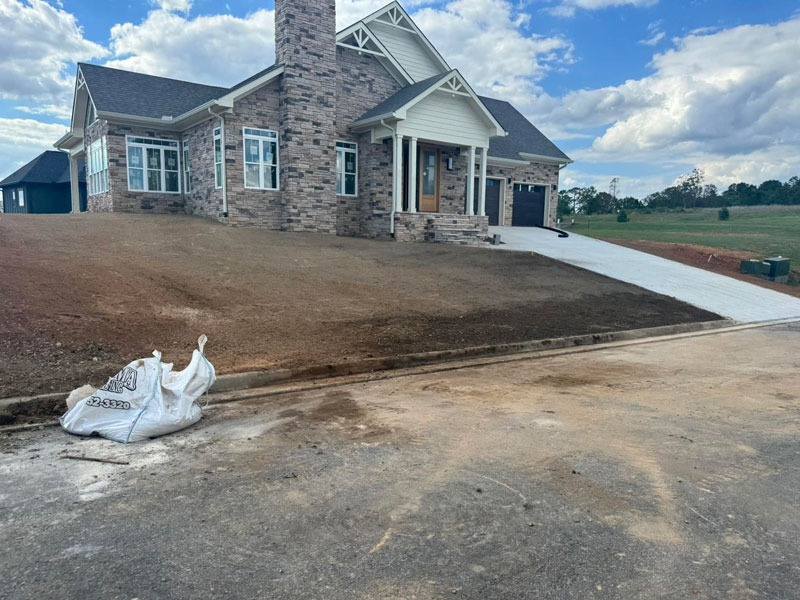 Freshly graded yard surrounding a new home beside a concrete driveway