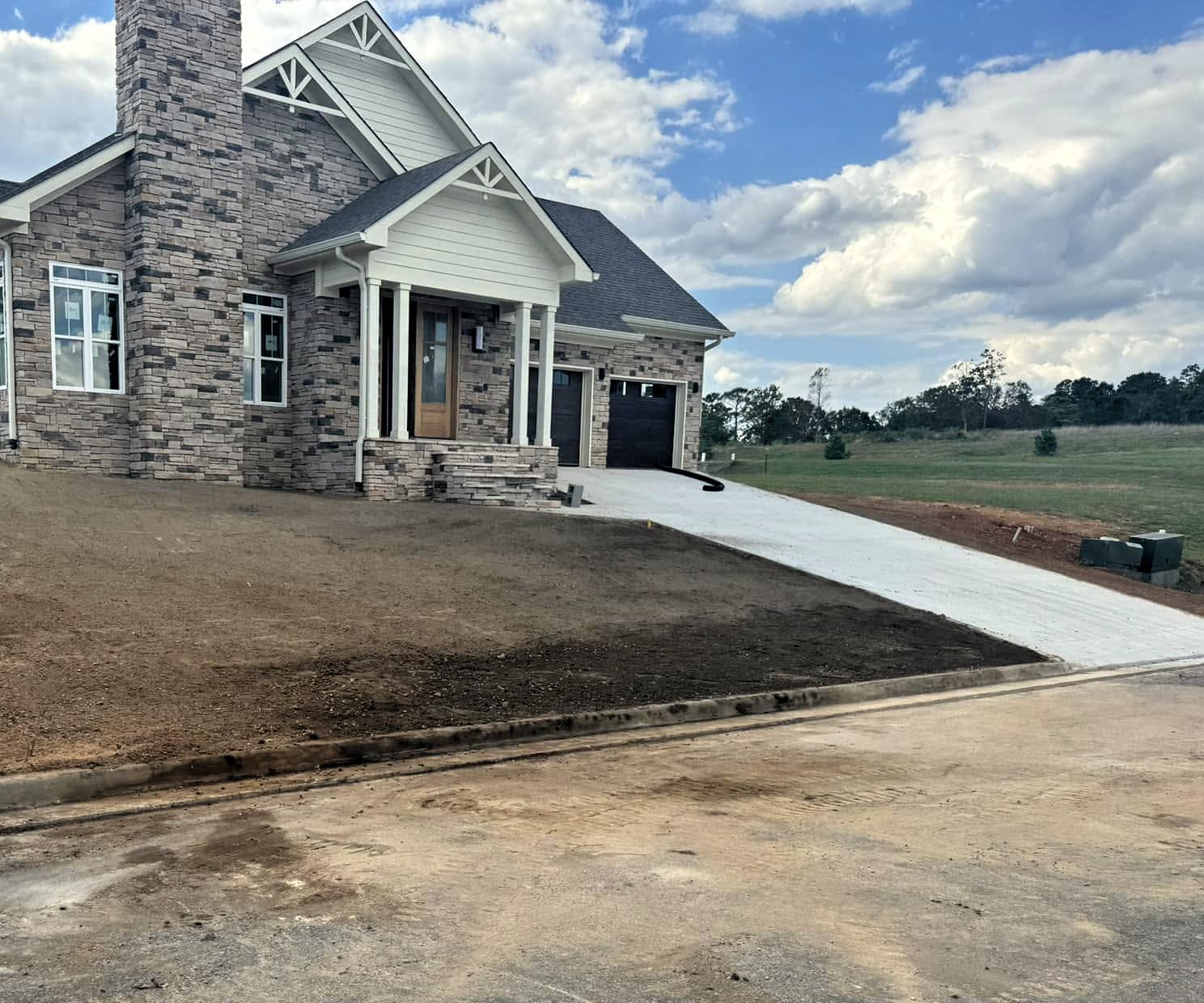 Concrete driveway and graded front yard beside a stone and siding home